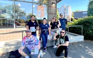 Picture of PROTEC17 organizers and director standing in front of a building. They are posed with other union siblings from other unions like Starbucks Workers United. Everyone is smiling and wearing their union gear.