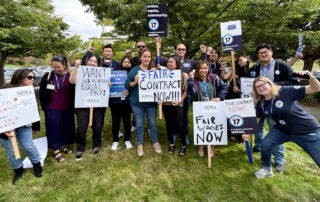 PROTEC17 members are joined by PROTEC17 staff and their WFSE and WPEA union siblings. Everyone is smiling and some folks are holding signs demanding a fair contract or raising their fists in solidarity. They are standing on the grass in front of big, green trees.