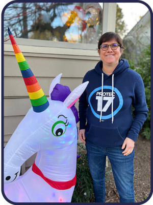 Picture of PROTEC17 member Alicia Brown in a PROTEC17 hoodie, posing with a blow up rainbow unicorn.